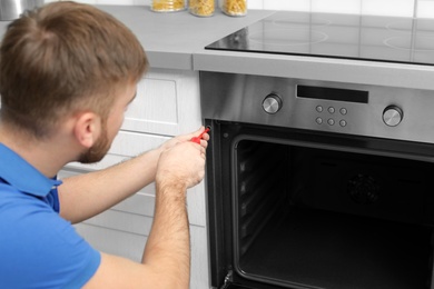 Professional serviceman repairing modern oven in kitchen