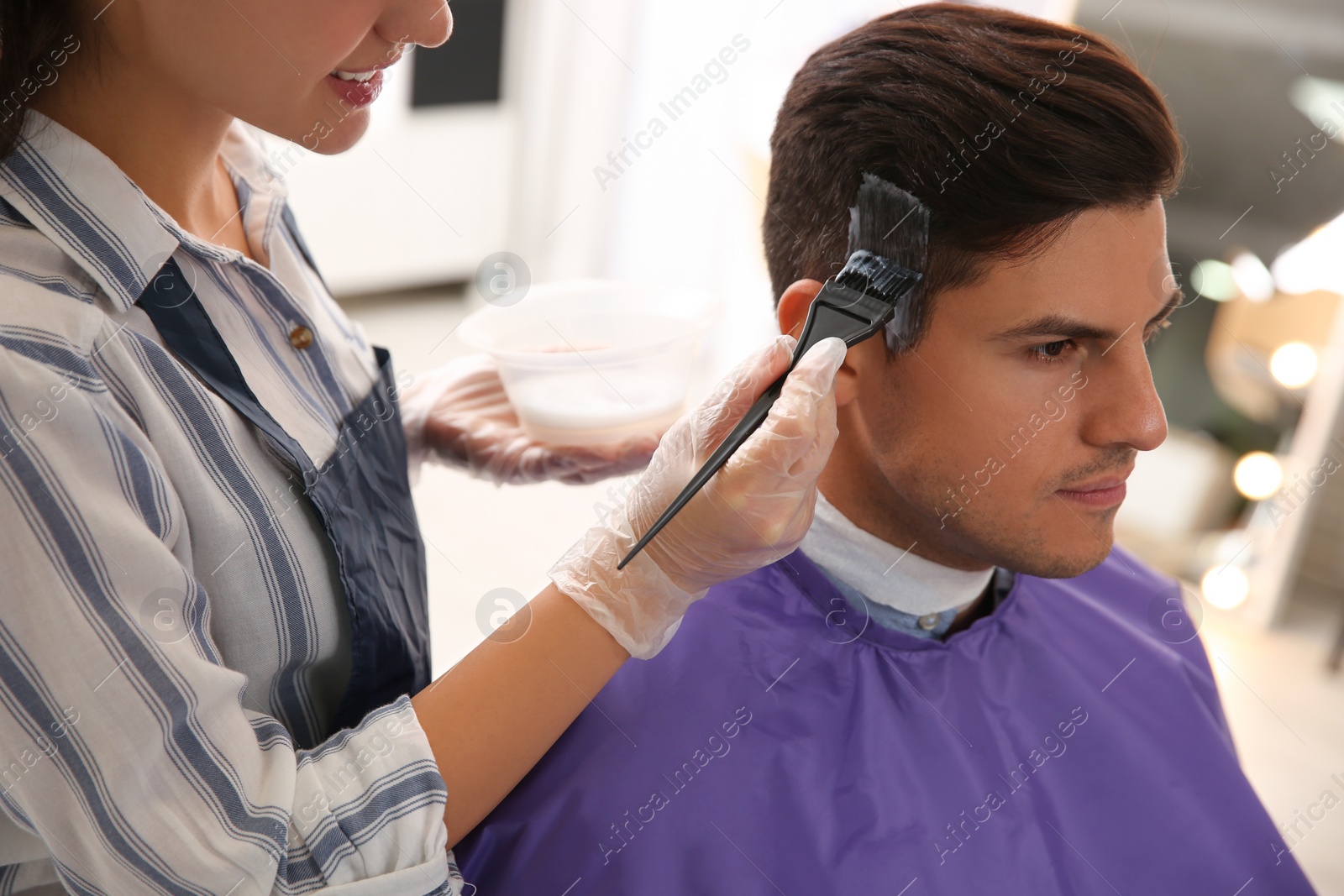 Photo of Professional hairdresser dying hair in beauty salon, closeup