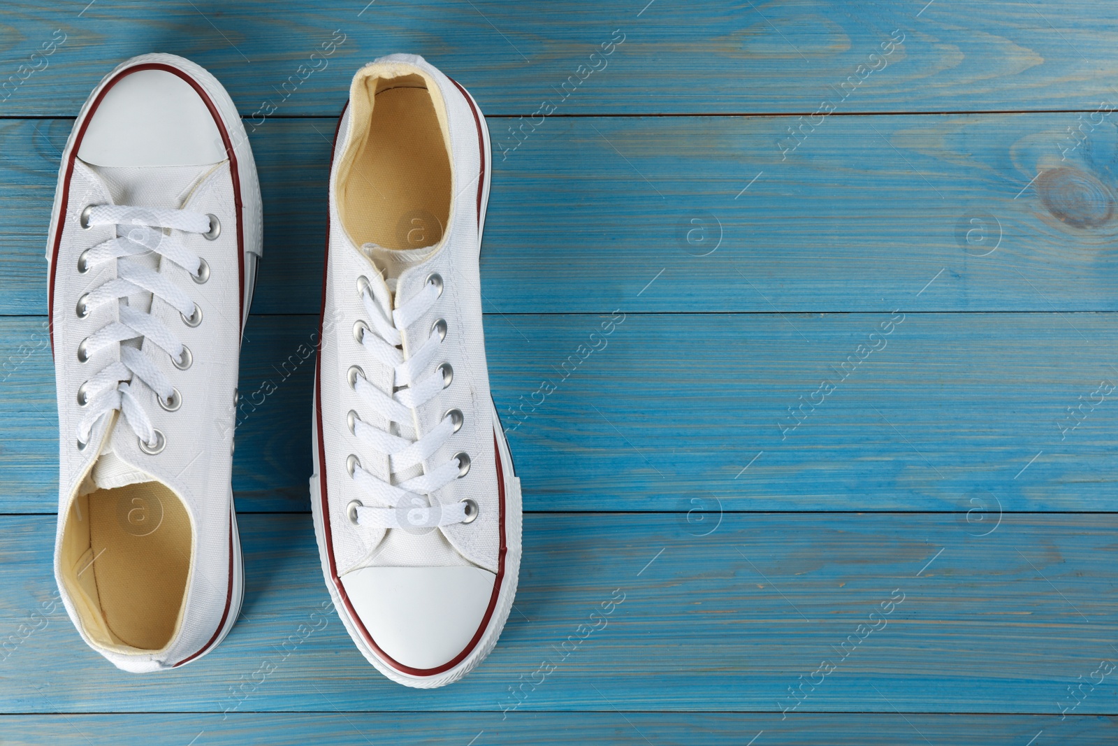 Photo of Pair of white sneakers on light blue wooden table, flat lay. Space for text