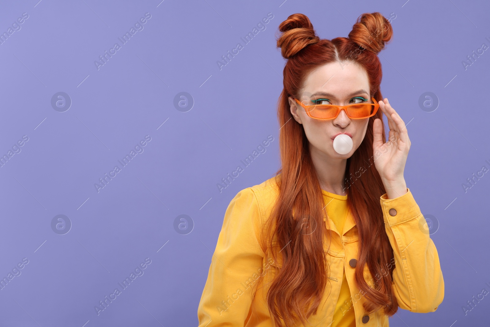 Photo of Portrait of beautiful woman in sunglasses blowing bubble gum on violet background. Space for text