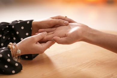 Photo of Chiromancer reading lines on woman's palm at table, closeup