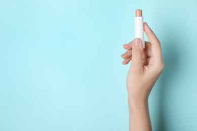 Woman holding hygienic lipstick on turquoise background, closeup. Space for text