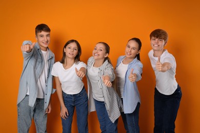 Group of happy teenagers showing thumbs up on orange background