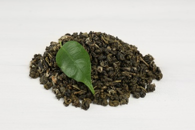 Photo of Heap of dried green tea leaves on white wooden table