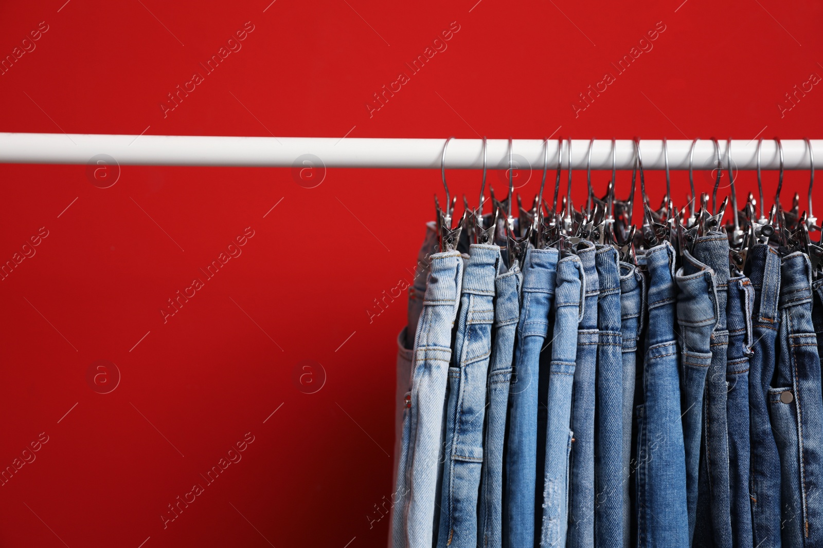 Photo of Rack with stylish jeans on red background