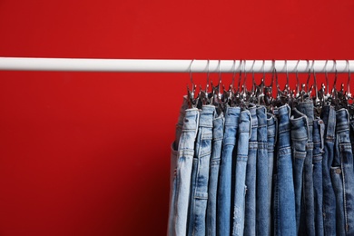 Rack with stylish jeans on red background