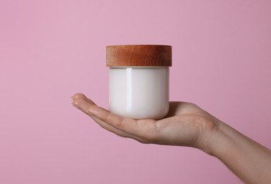 Woman holding jar of cosmetic product on pink background, closeup