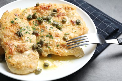 Photo of Delicious chicken piccata with herbs served on grey table, closeup