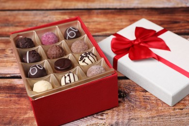 Photo of Red box with tasty chocolate candies on wooden table, closeup