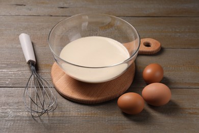 Photo of Metal whisk, dough in bowl and eggs on wooden table