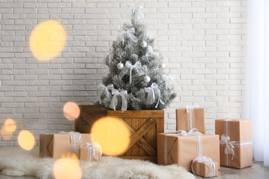 Photo of Stylish room interior with beautiful Christmas tree and gifts near white brick wall. Bokeh effect