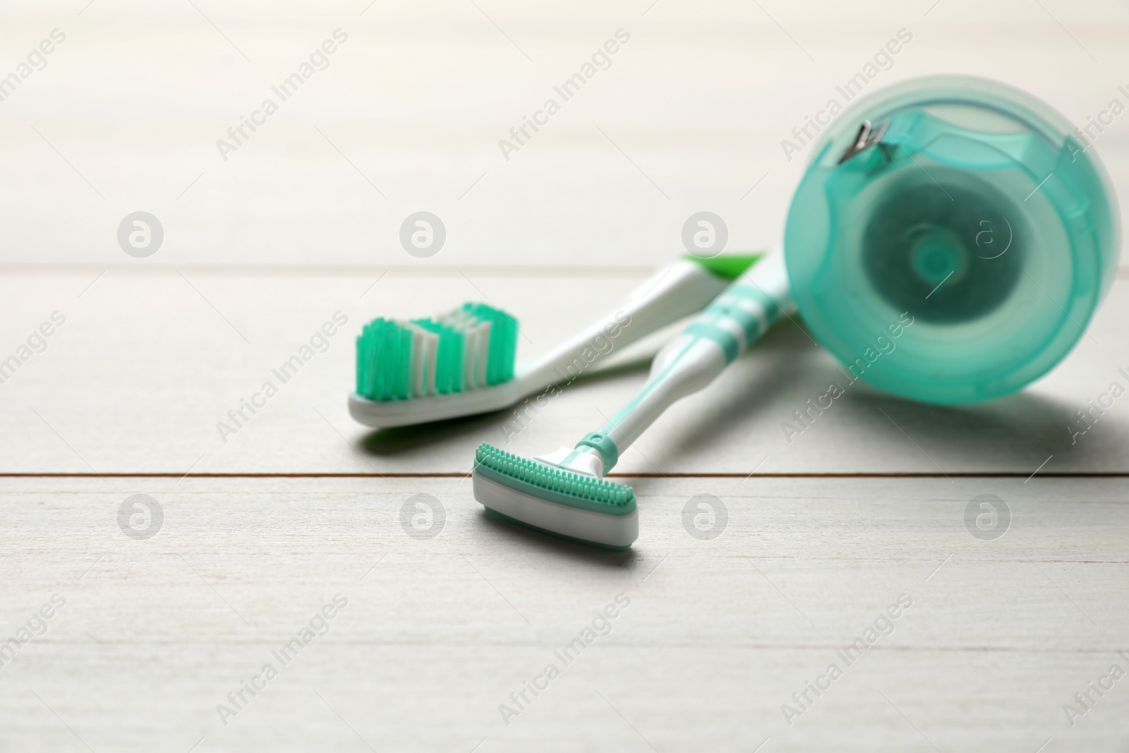 Photo of Tongue cleaner, toothbrush and dental floss on white wooden table, closeup