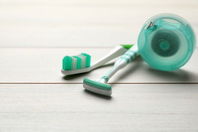 Photo of Tongue cleaner, toothbrush and dental floss on white wooden table, closeup