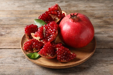 Photo of Plate with ripe pomegranates and seeds on wooden background