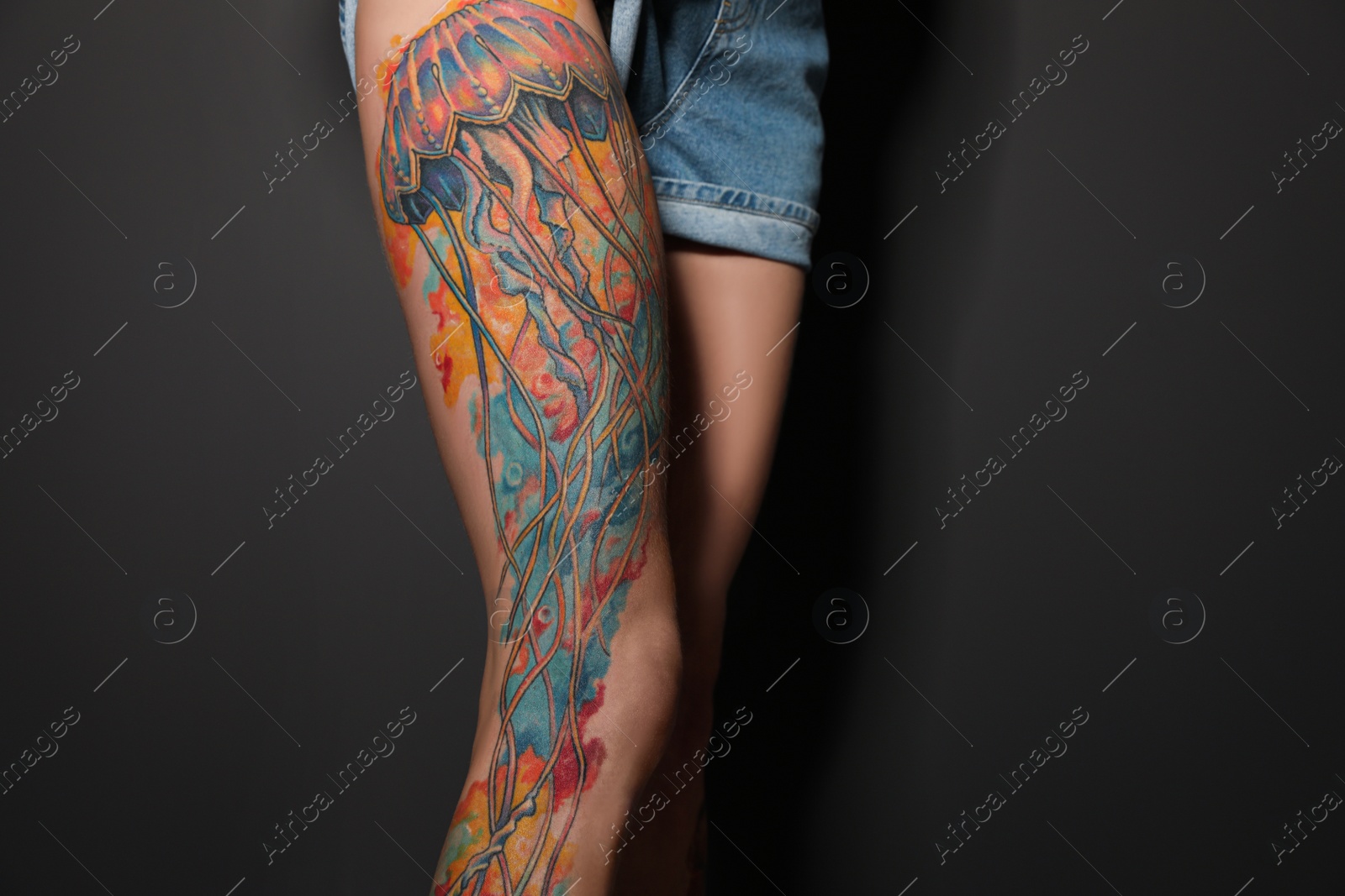 Photo of Woman with tattoos on leg against black background, closeup