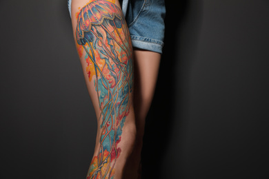 Photo of Woman with tattoos on leg against black background, closeup