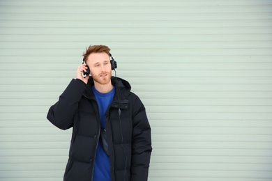 Young man listening to music with headphones against light wall. Space for text