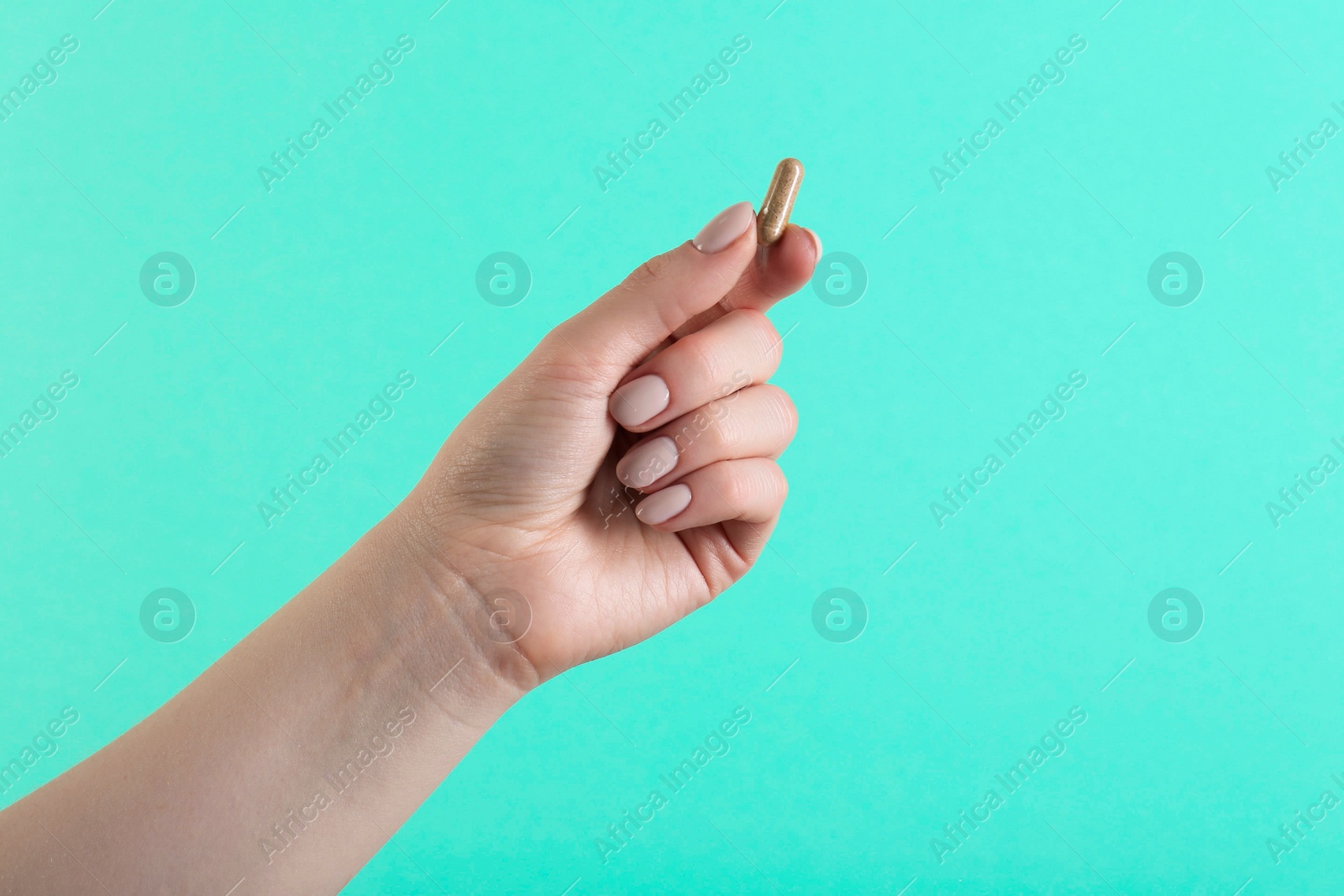 Photo of Woman holding vitamin capsule on turquoise background, closeup. Health supplement