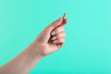 Woman holding vitamin capsule on turquoise background, closeup. Health supplement