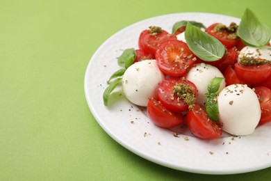 Photo of Tasty salad Caprese with tomatoes, mozzarella balls and basil on green background, closeup. Space for text