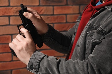 Dangerous criminal with gun near brick wall, closeup. Armed robbery