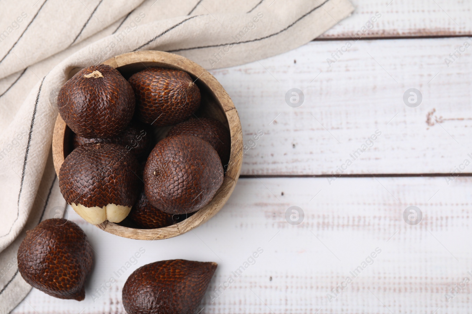 Photo of Fresh salak fruits in bowl on white wooden table, top view. Space for text