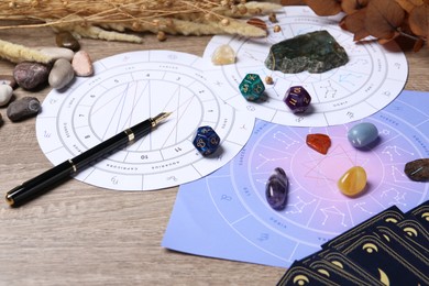 Zodiac wheels, natal chart, astrology dices and gemstones on wooden table, closeup