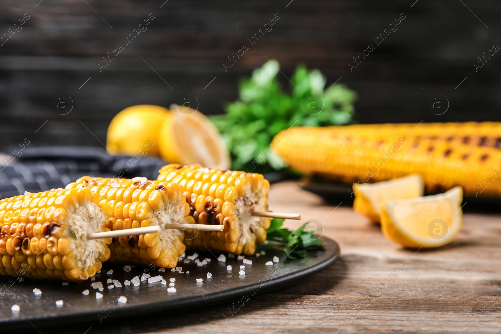 Photo of Slate plate with grilled corn cobs on wooden table, closeup. Space for text