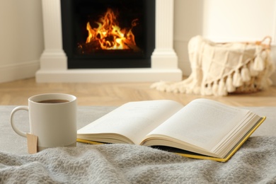 Photo of Cup of hot tea and book near fireplace at home. Cozy atmosphere