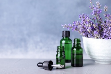 Photo of Bottles of essential oil and bowl with lavender flowers on stone table against blue background. Space for text