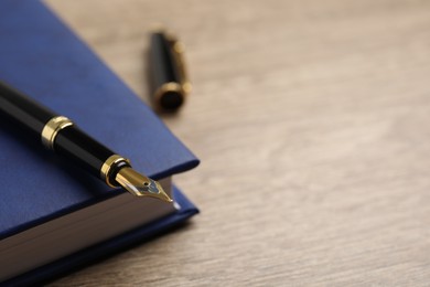 Photo of Beautiful fountain pen and blue notebook on wooden table, closeup. Space for text