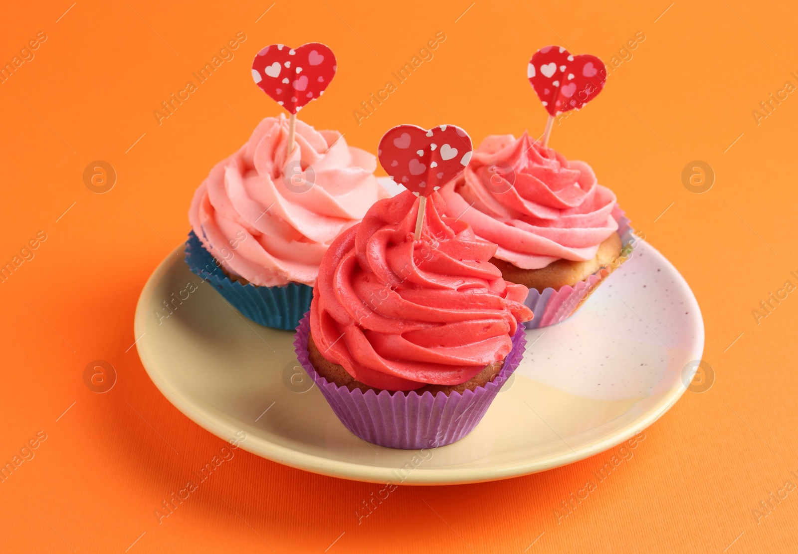 Photo of Delicious cupcakes with bright cream and heart toppers on orange background