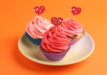 Delicious cupcakes with bright cream and heart toppers on orange background