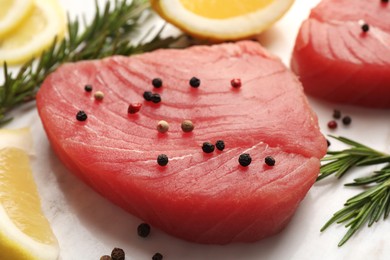 Raw tuna fillet with peppercorns, lemon and rosemary on white table, closeup
