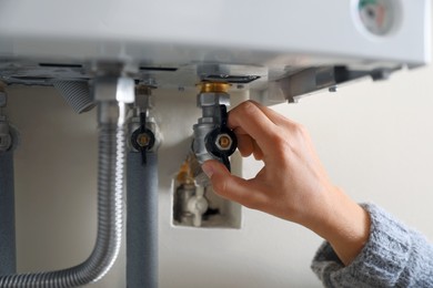Photo of Woman turning on valve of gas boiler, closeup