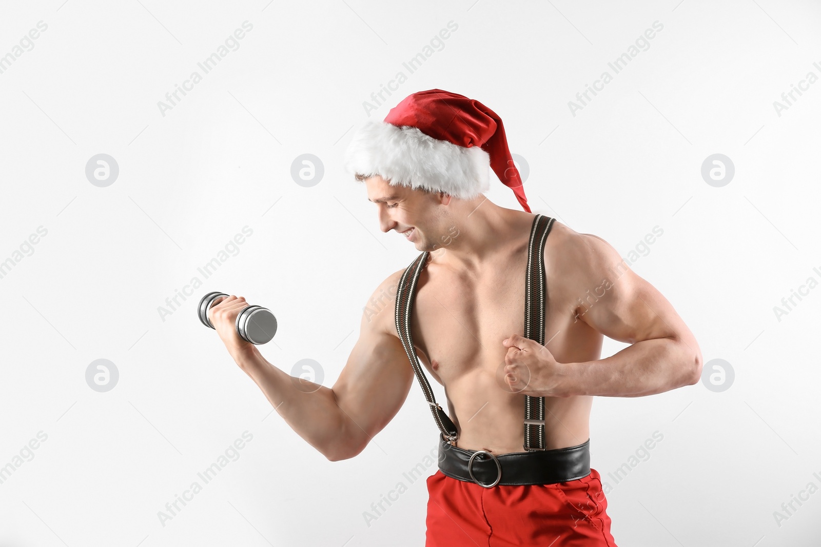 Photo of Young muscular man in Santa Claus hat with dumbbell on white background