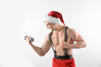 Photo of Young muscular man in Santa Claus hat with dumbbell on white background