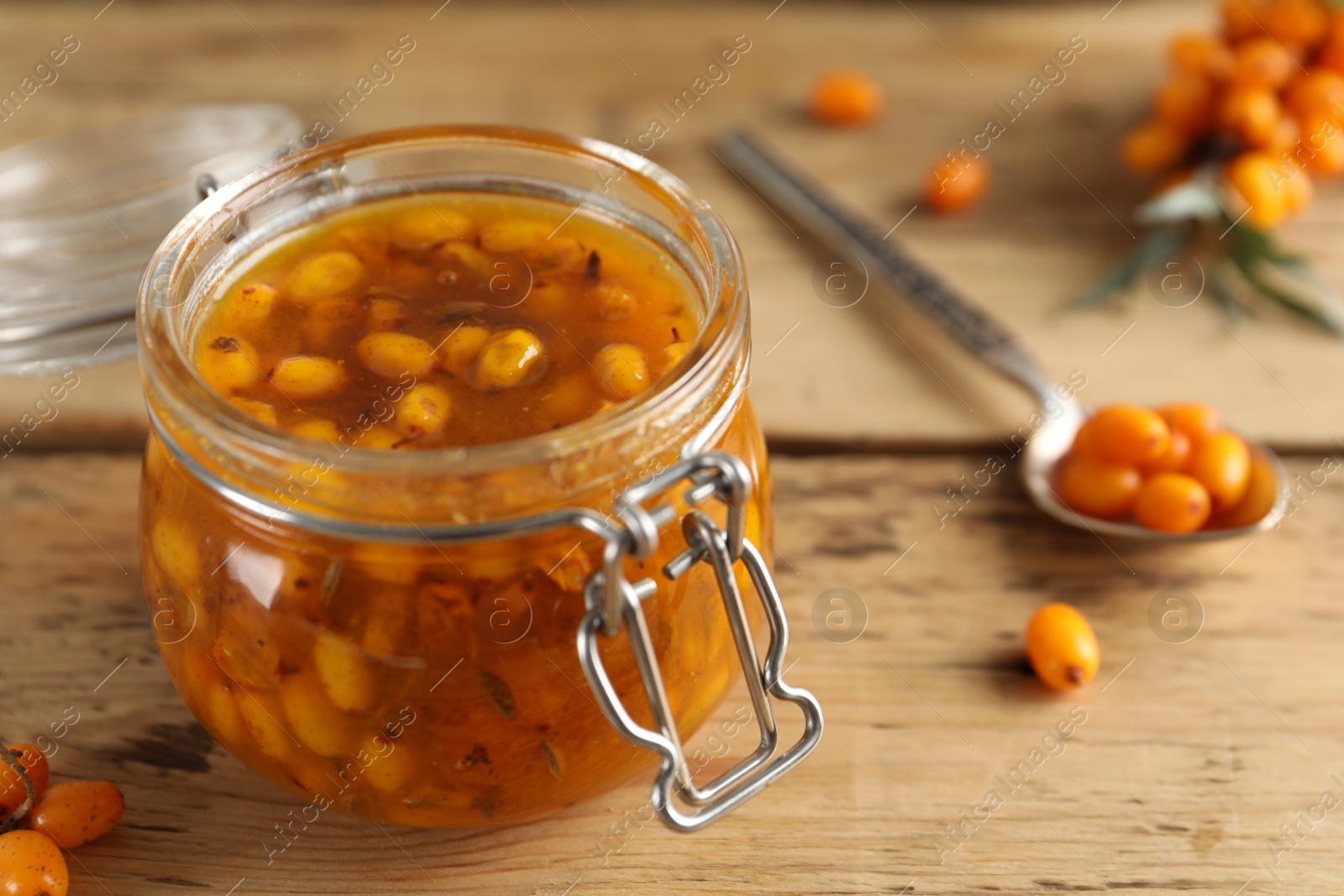 Photo of Delicious sea buckthorn jam and fresh berries on wooden table, closeup. Space for text