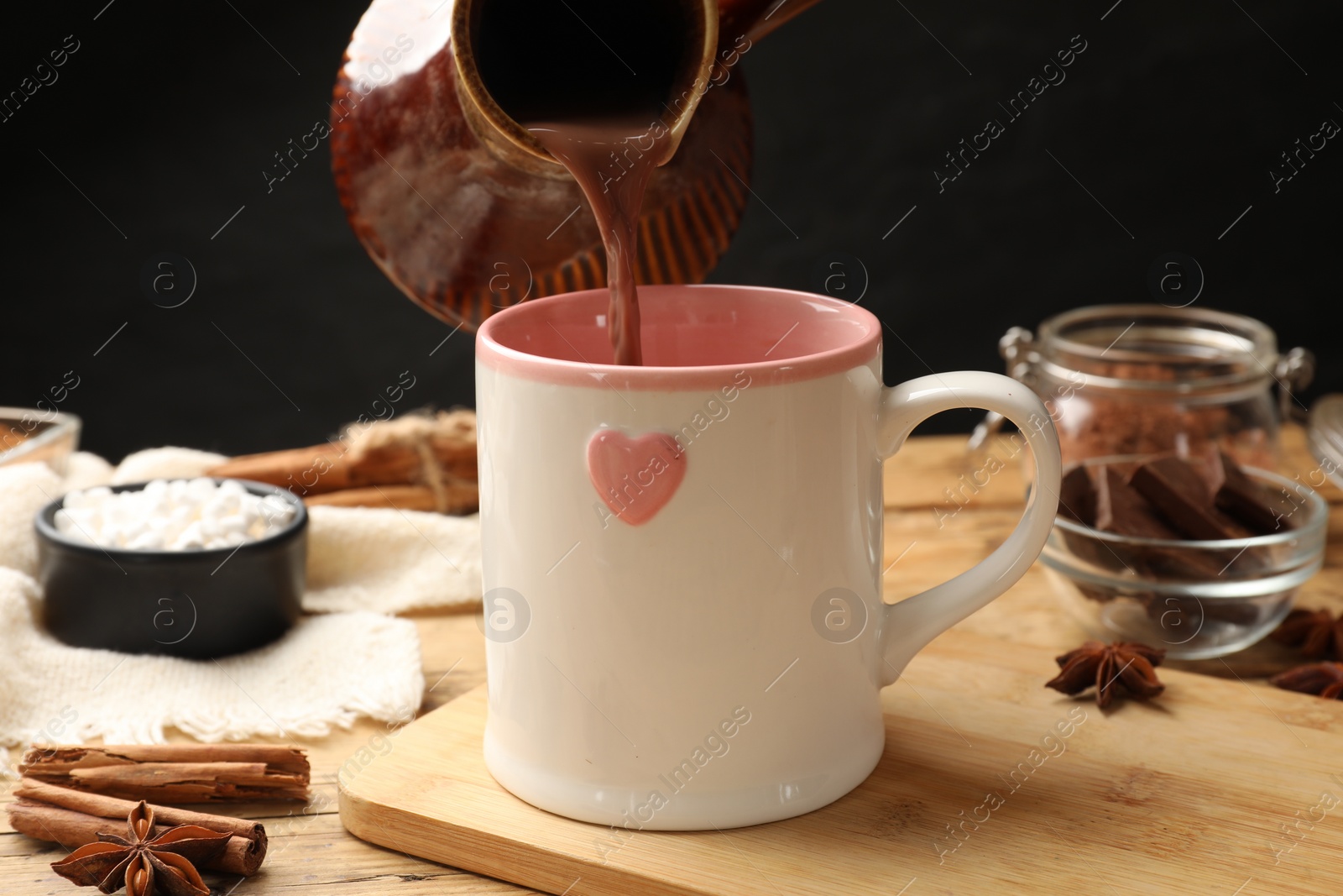 Photo of Pouring tasty hot chocolate into cup at wooden table, closeup