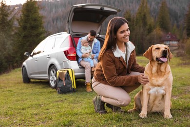 Photo of Happy woman with dog, father and his daughter sitting in car trunk outdoors. Family traveling with pet