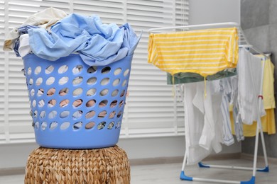 Photo of Plastic laundry basket with clothes on wicker pouf indoors. Space for text