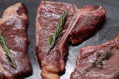 Photo of Fresh raw beef cuts with herbs on light grey textured table, closeup