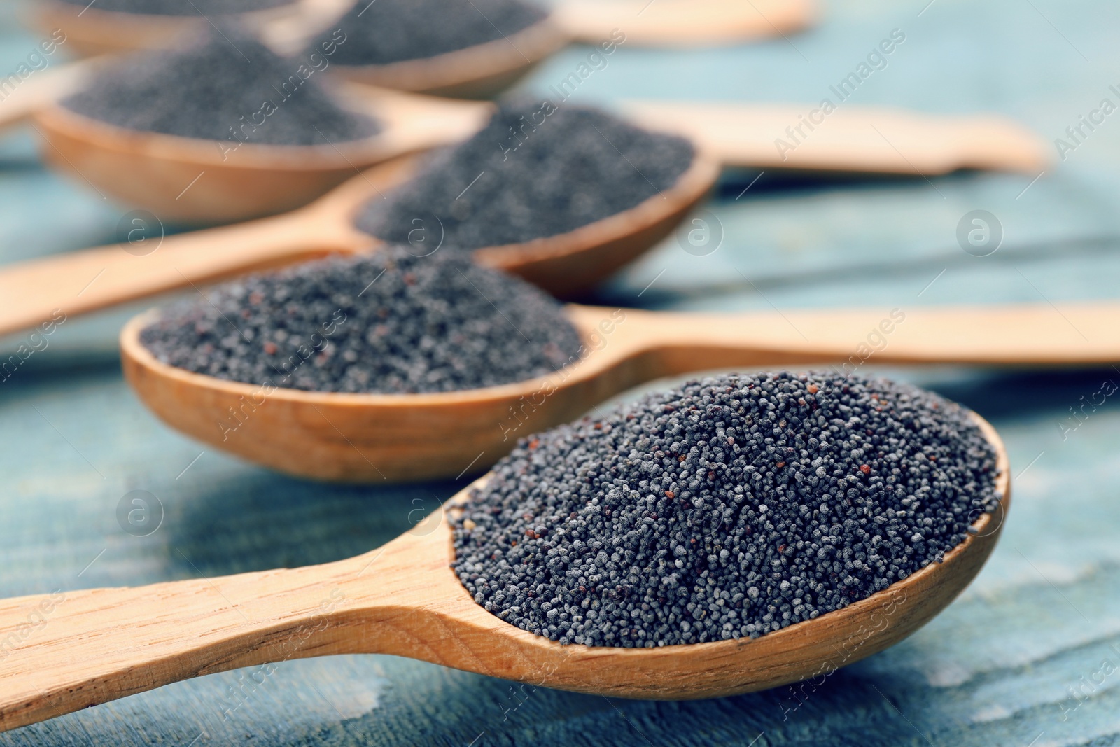 Photo of Poppy seeds in spoons on blue wooden table, closeup