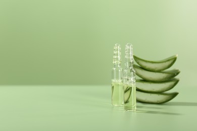 Skincare ampoules with extract of aloe vera and cut leaves on pale green background. Space for text