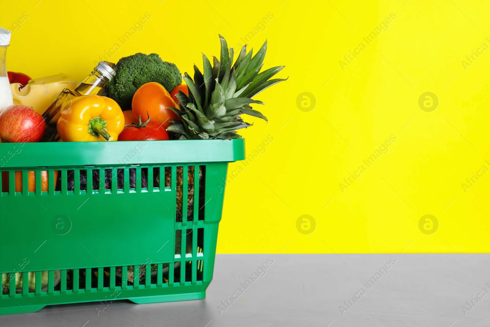 Photo of Shopping basket with grocery products on grey table against yellow background. Space for text