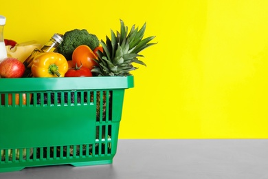 Photo of Shopping basket with grocery products on grey table against yellow background. Space for text