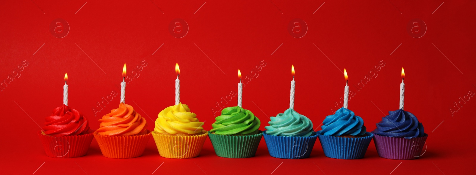 Photo of Delicious birthday cupcakes with candles on red background