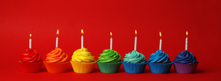 Delicious birthday cupcakes with candles on red background