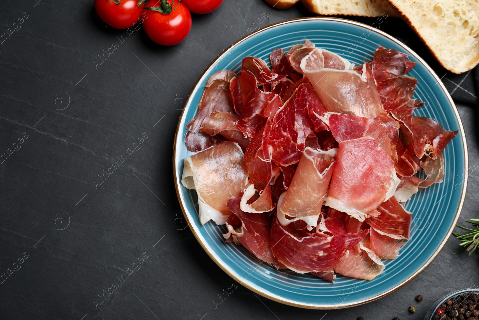 Photo of Tasty prosciutto served on black table, flat lay