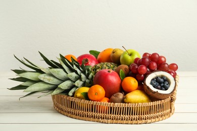 Wicker tray with different fresh fruits on white wooden table